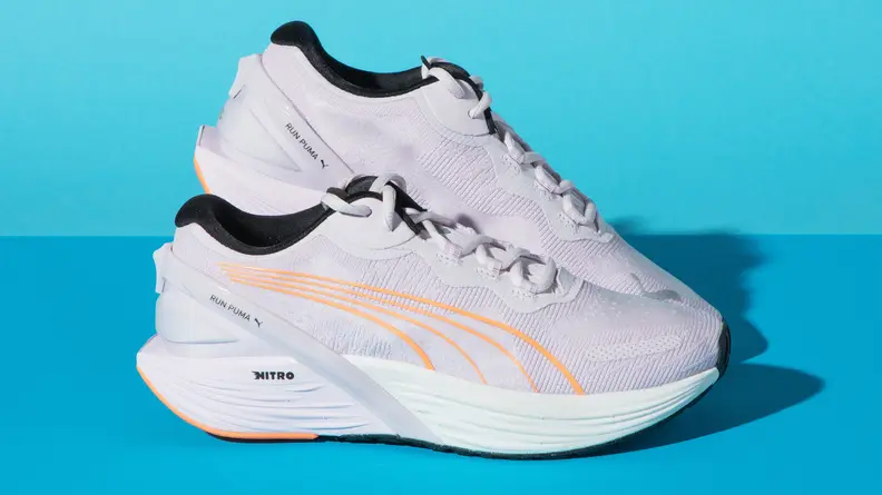 A pair of white Puma Run XX Nitro surrounded by a blue background.