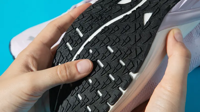 A person touches the black outsole of a running shoe.