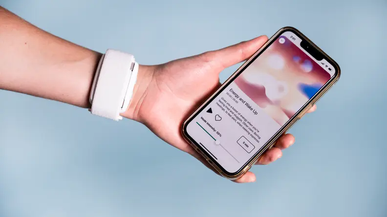 A person holds a cell phone while wearing a white stress tracker on their wrist.