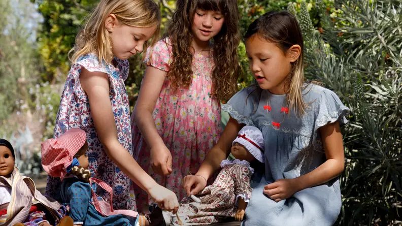 Three girls having a tea party with their American Girl dolls