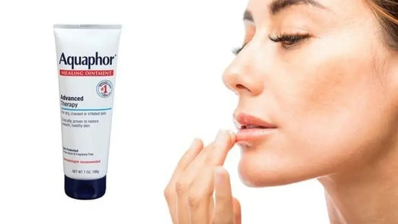 Close-up of a woman applying Aquaphor healing ointment to her lips.