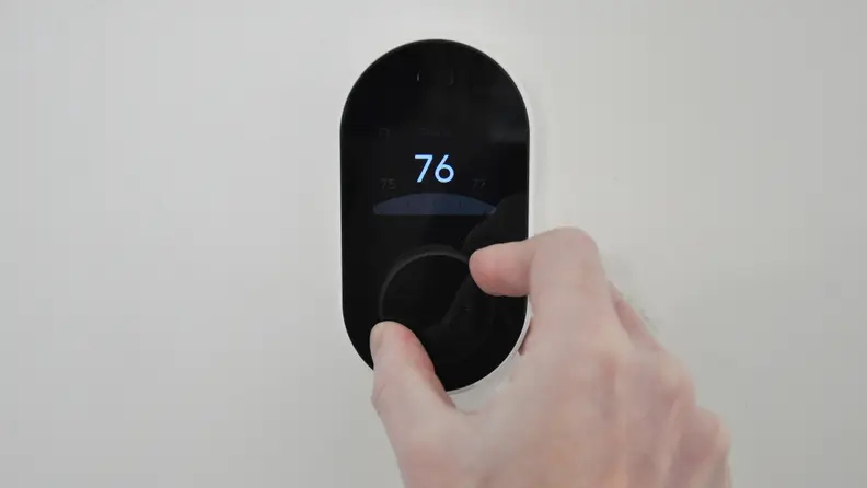 Black Wyze Thermostat mounted against white wall. Display shows 