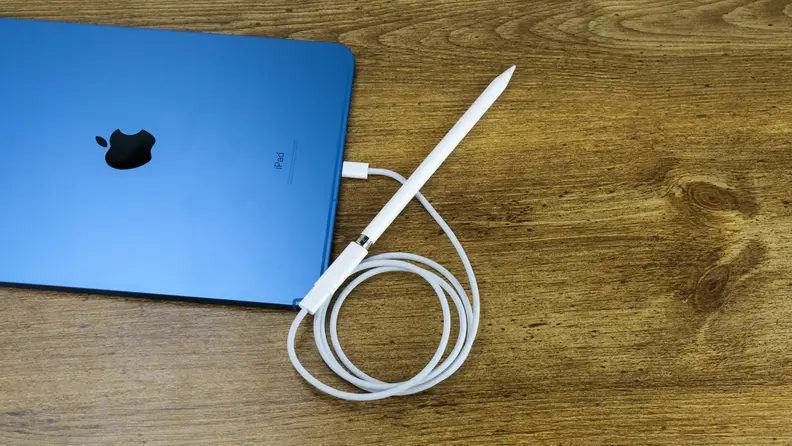 The blue Apple iPad 10 sits on a wooden desk with an Apple Pencil plugged in.