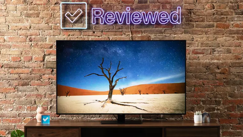 Samsung Q80B TV in front of brick wall under neon sign indoors with desert setting on screen.