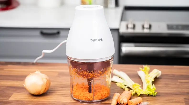 The Philips mini food processor is seen on a kitchen counter, with some onions, and other vegetables scattered around.