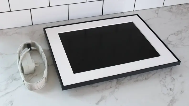 The Aura Walden digital photo frame unboxed with its beige charging cable beside it.
