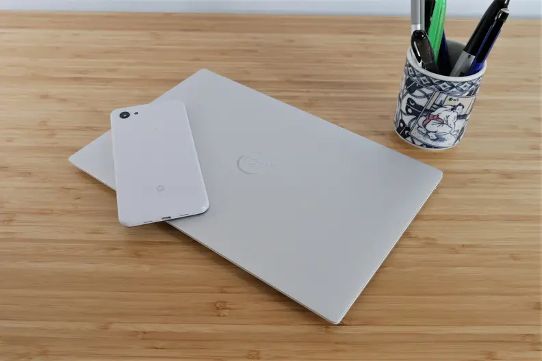 A closed laptop on top of a desk with a cell phone on top and a cup of pens behind it.