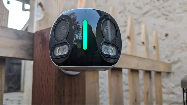 The Lorex 4K Dual-Lens Wi-Fi Security Camera hanging on a fence post outdoors.