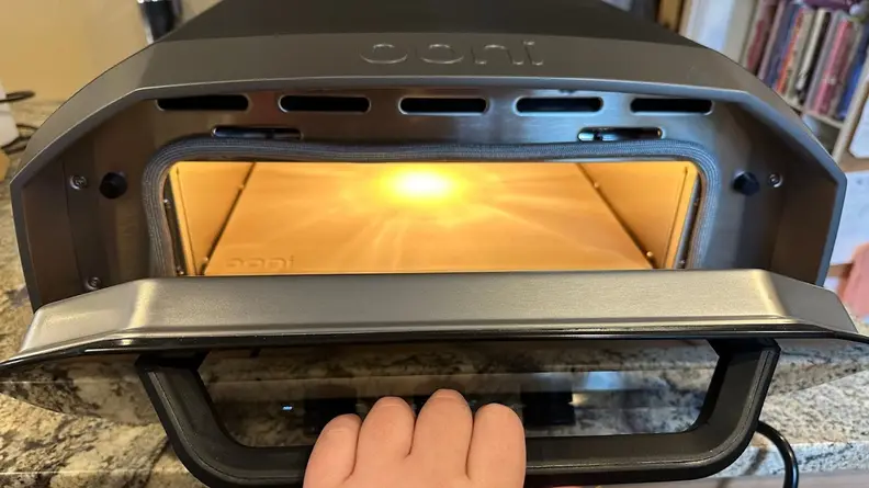 Person opening door on the Ooni Volt 12 pizza oven on top of granite countertop.
