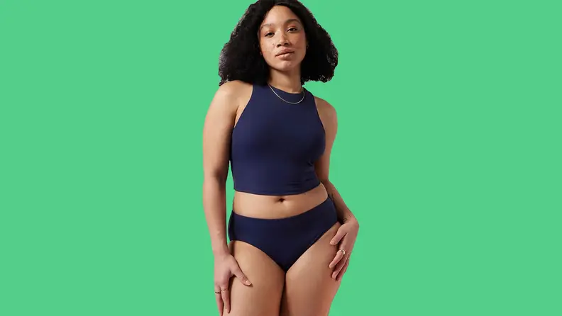 Black woman wearing navy tankini on green background.