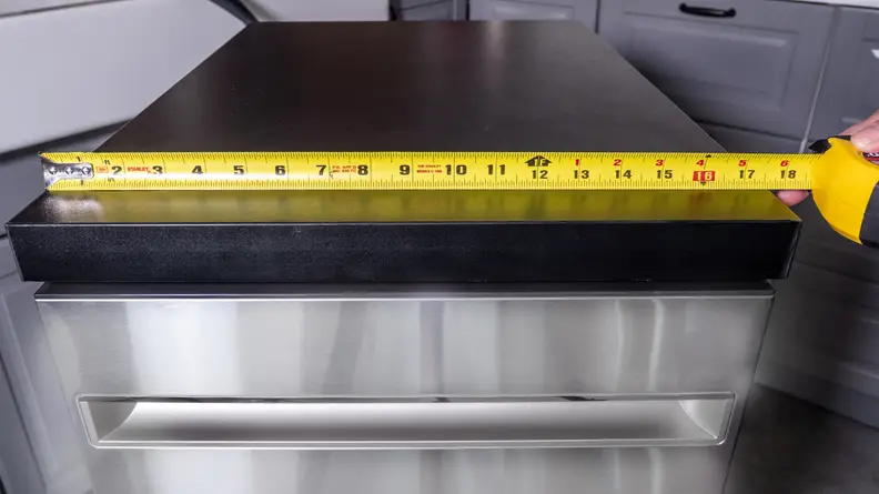 A tape measurer lies across the top of the GE GPT145SSLSS dishwasher, indicating itss a bit less than 18 inches wide.