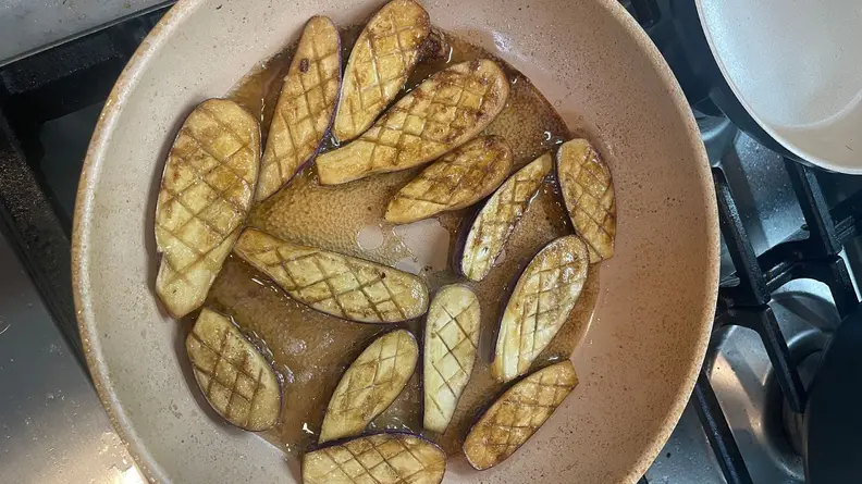 Seared eggplants cooking inside of nonstick skillet pan on cooktop.