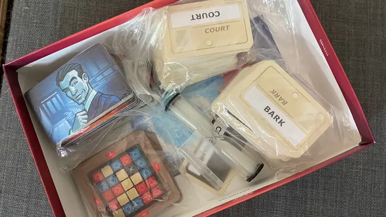 The box of Codenames with a timer, keyword cards, colored tiles for each team, and legends sits open.