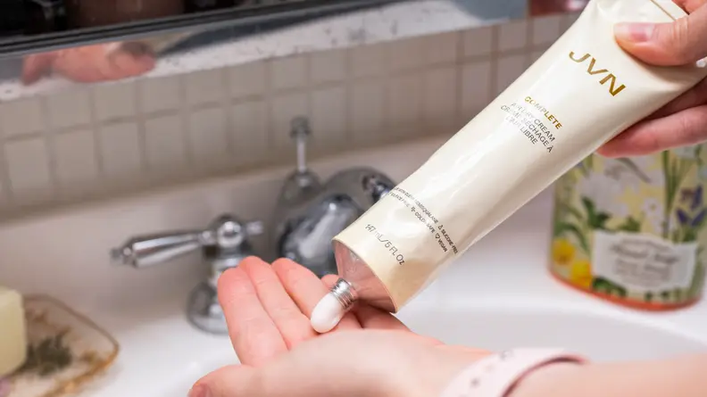 A hand squeezing a tube of hair cream into the other hand.