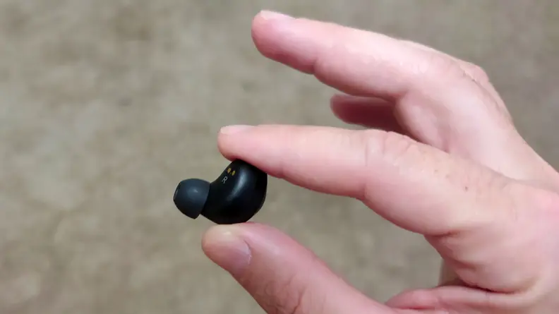 A hand is holding the all black Raycon earbud to show its diminutive size.
