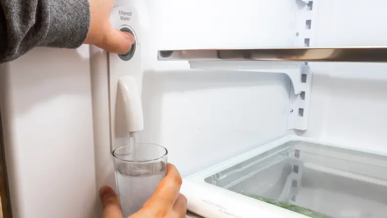 In close-up, someone pours a glass of water from a built-in refrigerator filter.
