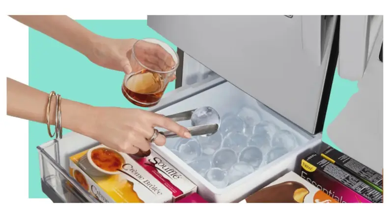 Person grabbing ball of ice to place inside of glass with tongs from bottom freezer drawer.