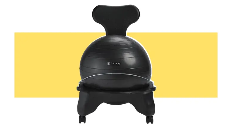 Black yoga ball sitting inside of black seat frame in front of yellow background.