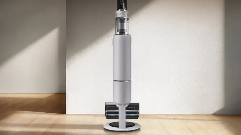 A stick vacuum stands in its dock up against a wall