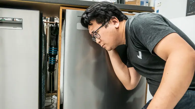 A person crouched down listening to a dishwasher.