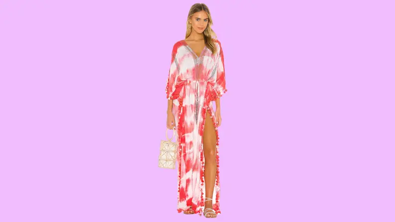 A model wearing a red and white caftan with strappy sandals and a raffia bag.