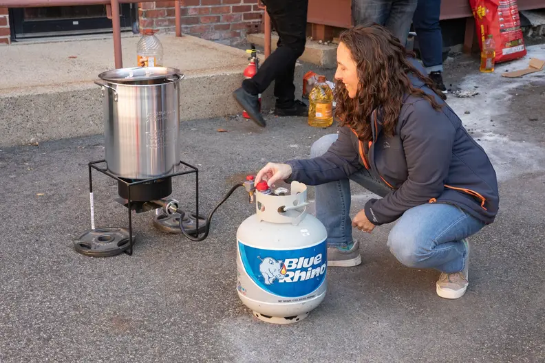 A person adjusts the propane tank connected to an outdoor deep fryer.