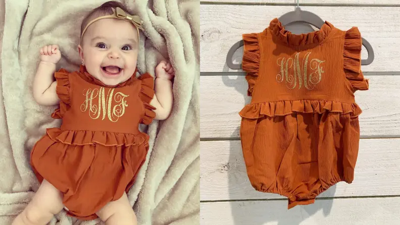A smiling baby in a romper with gold monogram