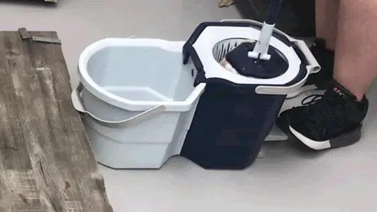 A human foot in sneakers presses the spin mop’s pedal with the spin mop inserted.