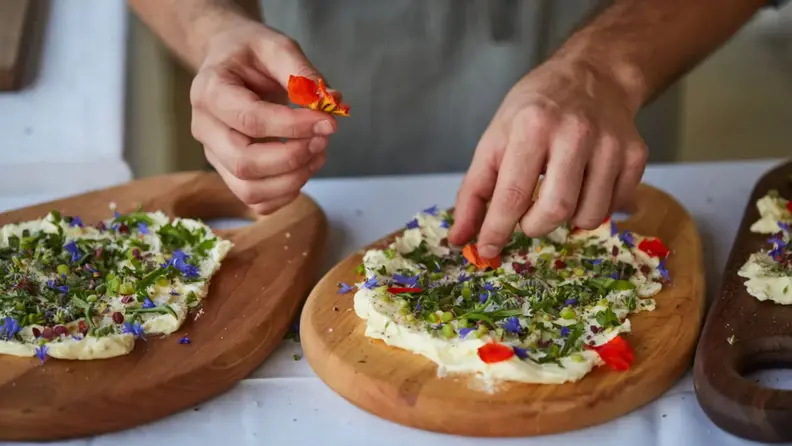 Hand placing toppings on a wooden cutting board smeared with butter