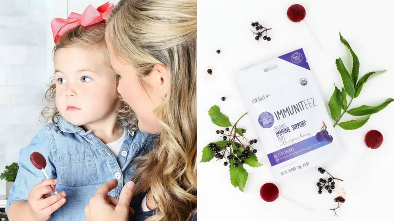 Left: A mother holds a young girl dressed in a blue shirt, holding an elderberry lollipop and looking off into the distance. Right: A top-down photo of a white bag of organic elderberry lollipops with elderberries and leaves surrounding it.