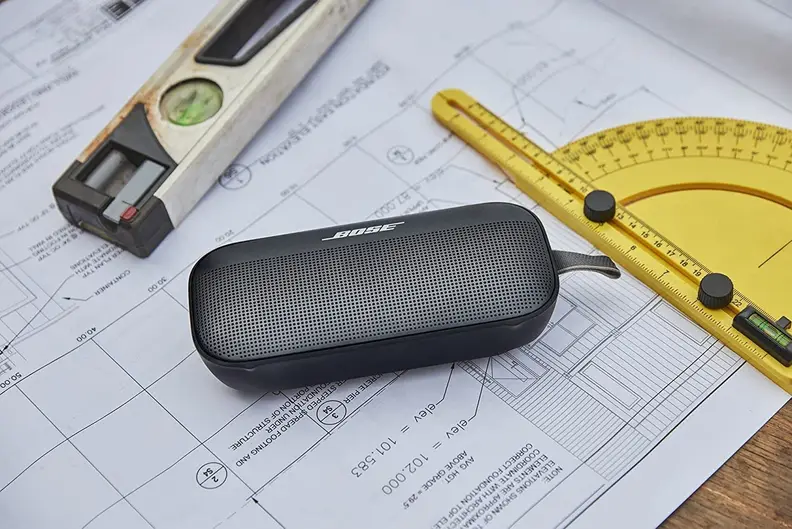 A Bose portable speaker sitting on some blueprints next to a protractor and a bubble level.
