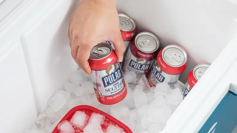 Someone putting a can of seltzer in an ice filled cooler.