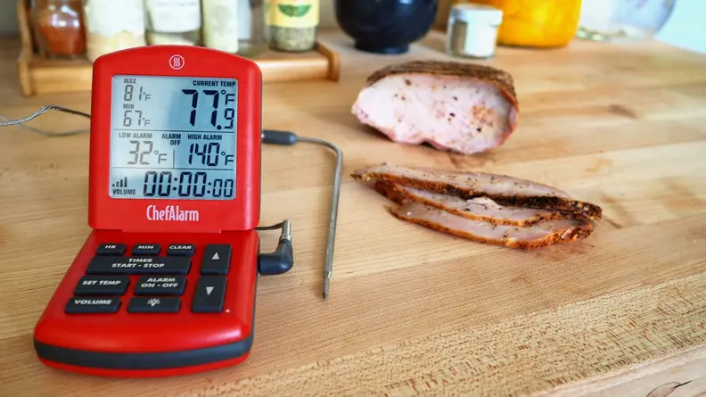 A probe thermometer sits on a kitchen counter next to freshly sliced brisket.