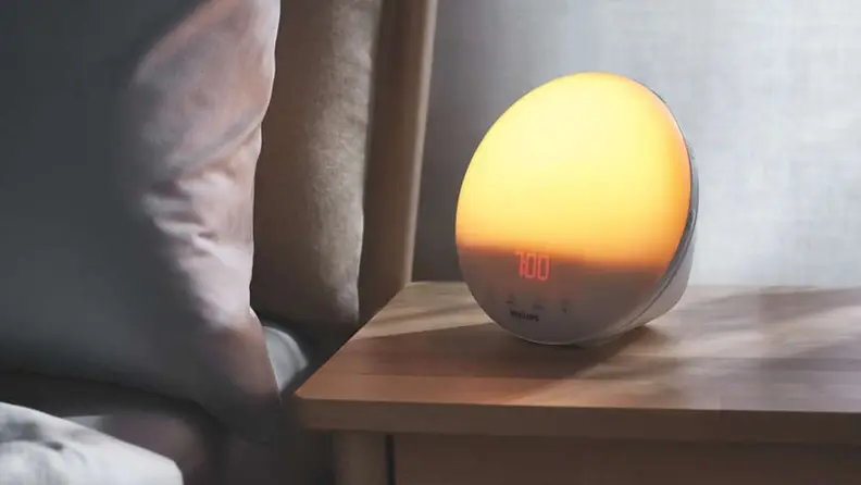 Alarm clock with built-in light sitting on bedside table next to bed.