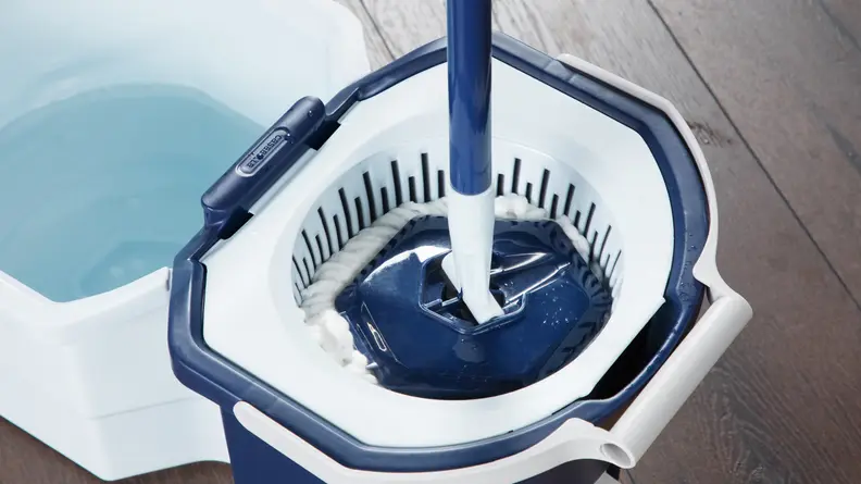 Mop inside of the spin bucket next to filled water reservoir on top of hardwood floor.
