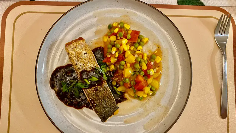 In the center of the plate, there's a piece of king salmon with skin on and a side of vegetable stir-fry.