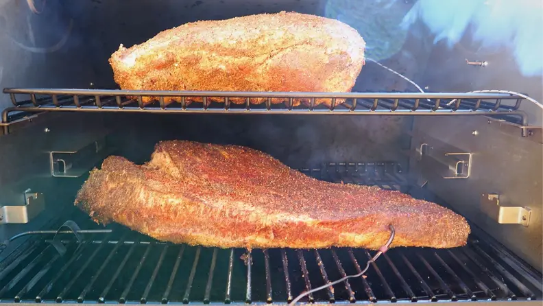 Two briskets being cooked in the Traeger grill with inserted probe thermometers