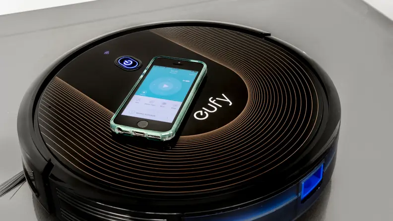 The Eufy Robovac 30C with a phone displaying its smart app atop it.