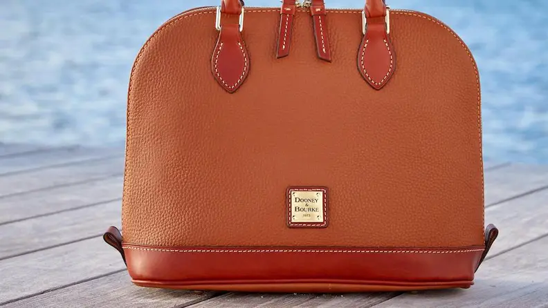 A leather Dooney & Bourke satchel on a pier with a water background.