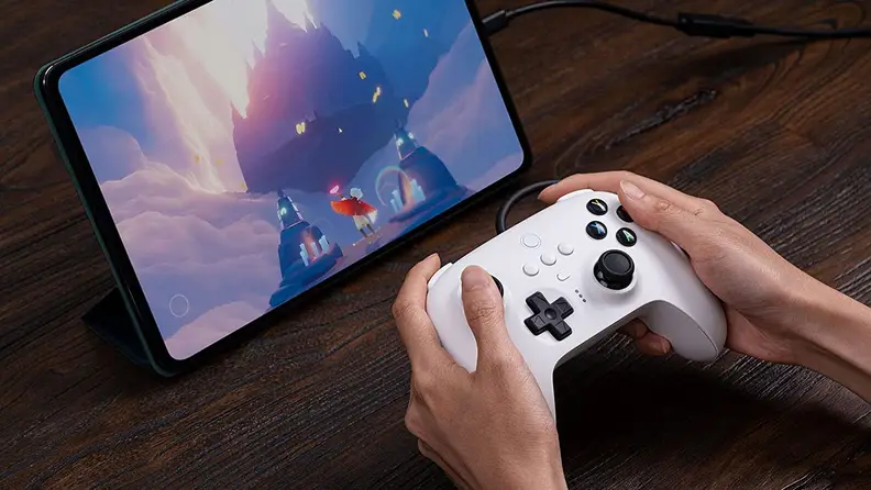 Someone playing a game on a tablet with the 8Bitdo Ultimate wired controller.