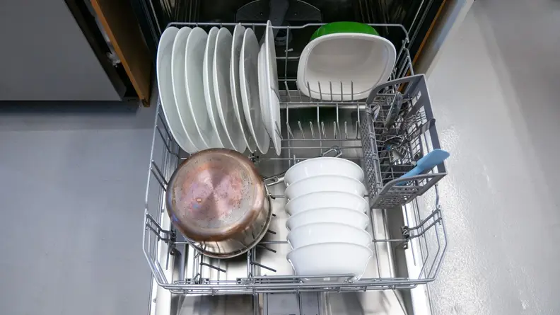 A close-up of the dishwasher's bottom rack, stocked with dishes. You can see a column of foldable tines folded down to make room for a large pot.