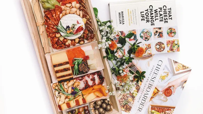 Aerial shot of Mezzo board with CheeseBoarder paper guide and Marissa Mullen's best-selling book beside it.