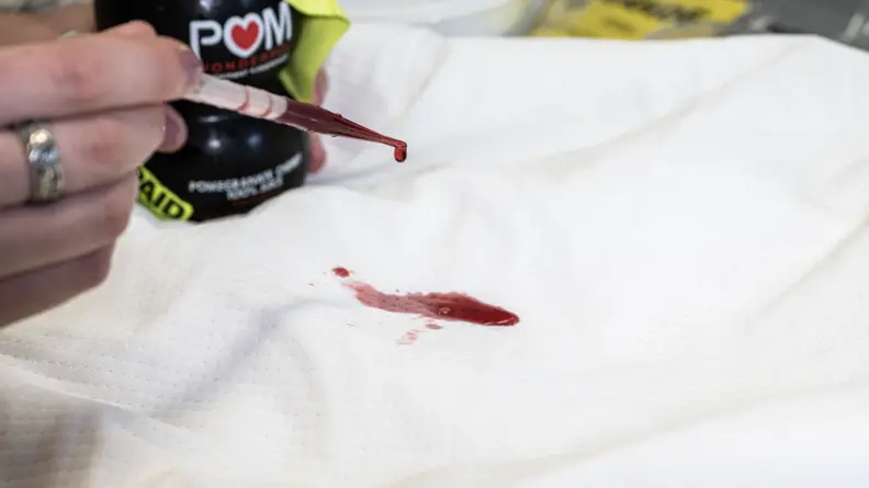 a pipette filled with red pomegranate juice drops liquid onto a mattress protector