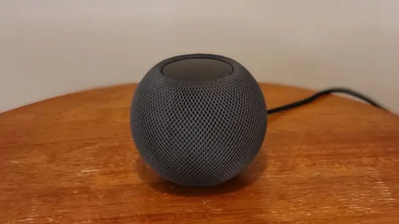 Apple's HomePod Mini smart speaker sits on a wood table.