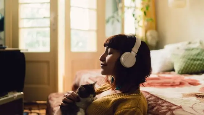 A person wearing headphones holds a kitten.