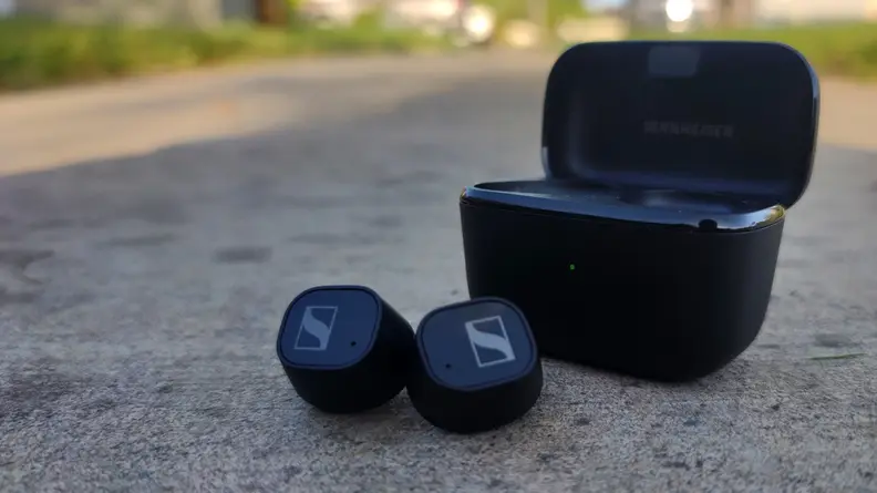 Sennheiser CX Plus all-black earbuds sitting on the ground with case in background.