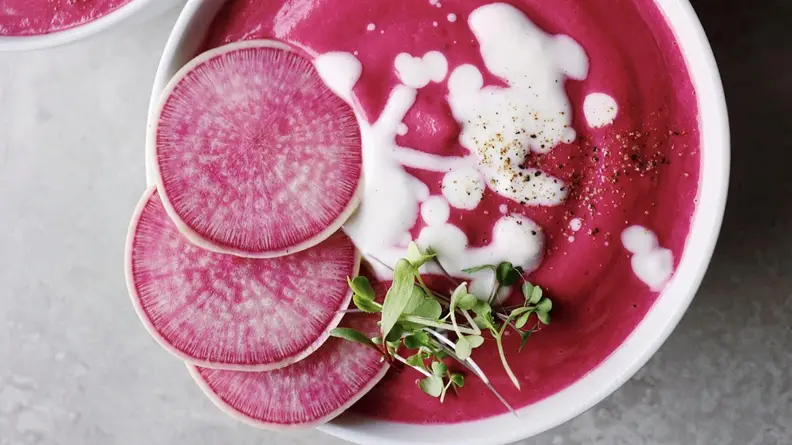 A bowl of bright pink soup garnished with radishes and white sauce