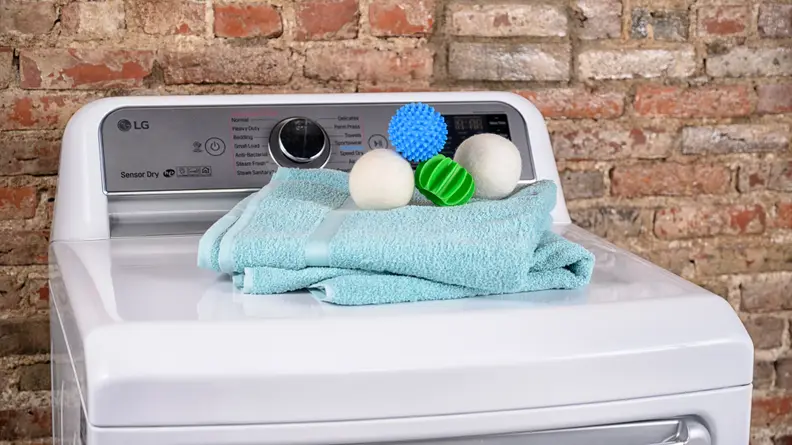 A variety of dryer balls and a blue towel are photographed on top of a top-loading dryer in our testing lab.