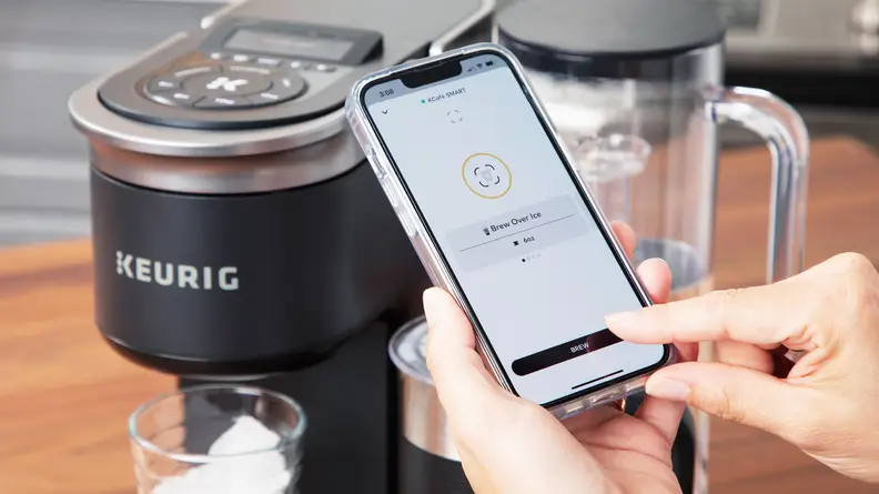 A close up of a person using the app on a smartphone to control the Keurig K-Cafe Smart coffee machine.