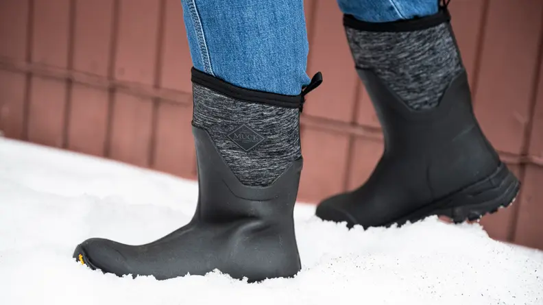 A woman wears a pair of Muck Boots Women’s Arctic Ice Mid-Height winter boots. She is standing in the snow.